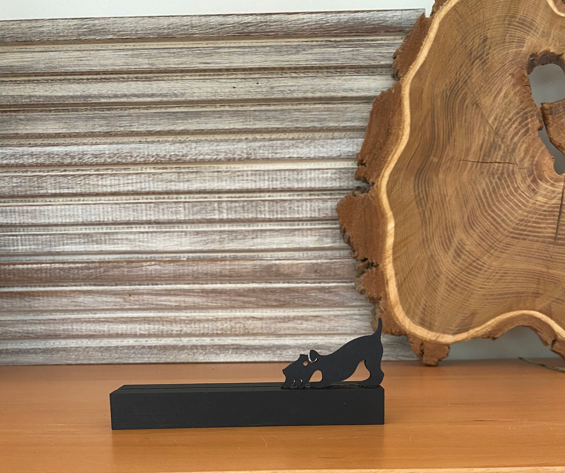 Zwart metalen hondenbeeldje op een rechthoekige voet; houten achtergrond.