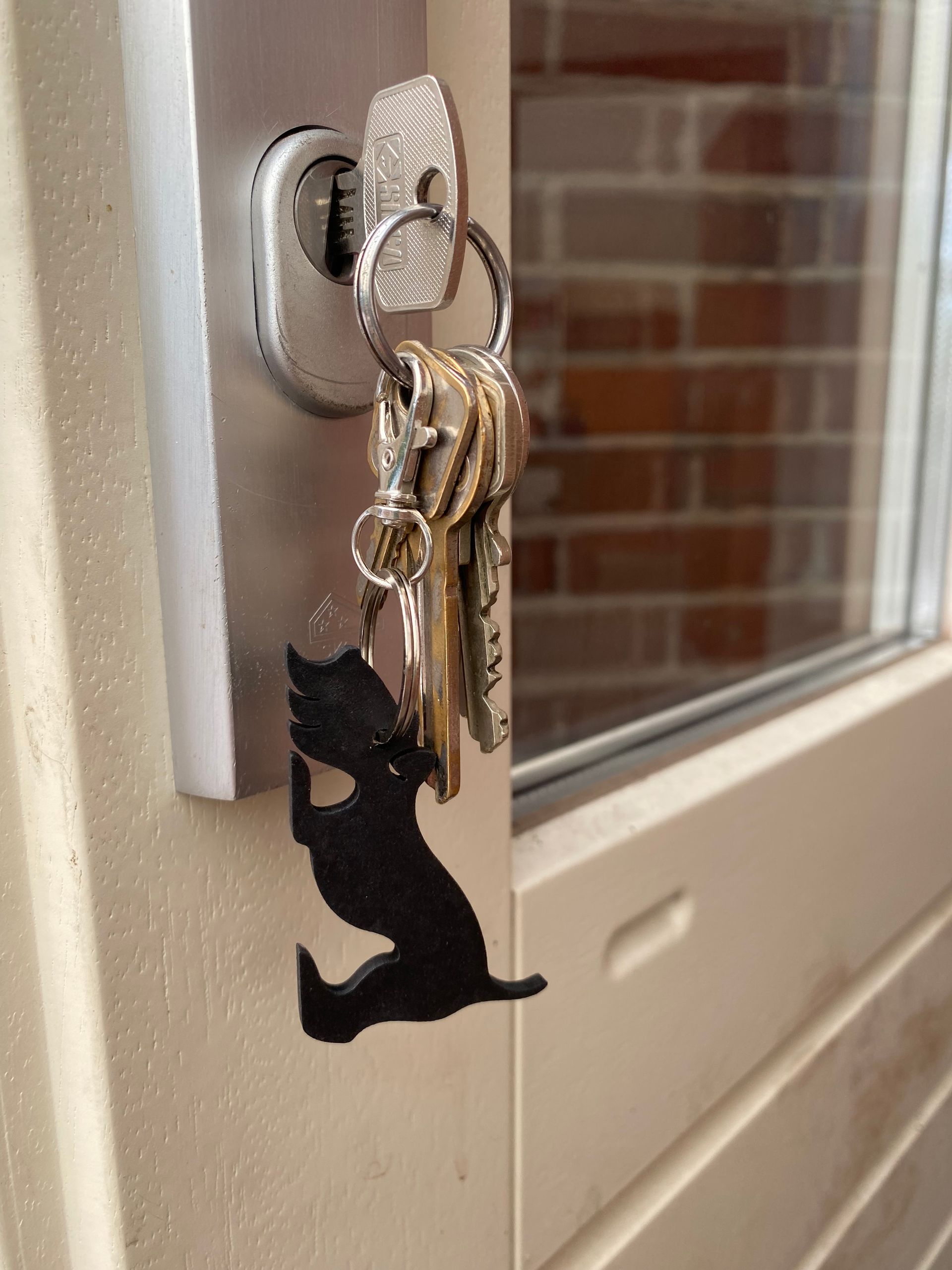 Sleutelhanger van een zwarte hond op een houten oppervlak, in een speelse houding met opgeheven staart.