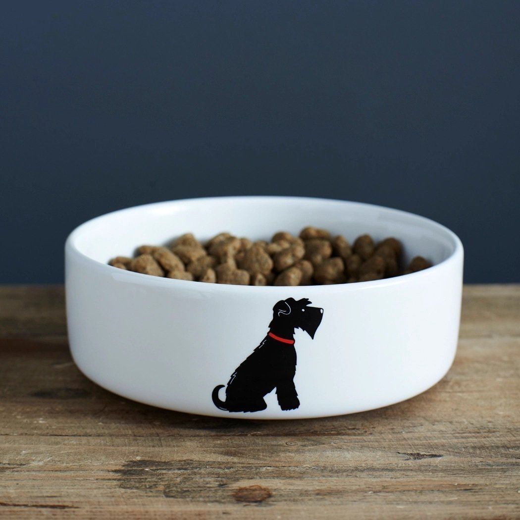 Witte hondenbak met silhouet van een zwarte hond, bruine doos en decoratief ei op een houten oppervlak.