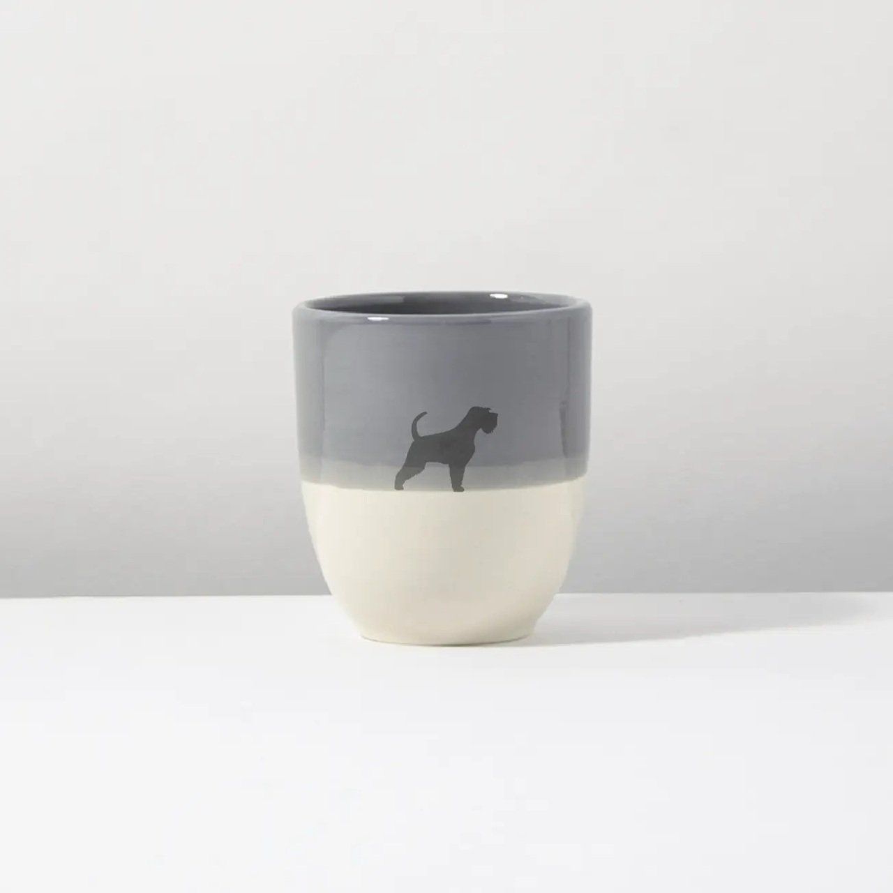Een grijs-witte kop met daarop het silhouet van een hond.