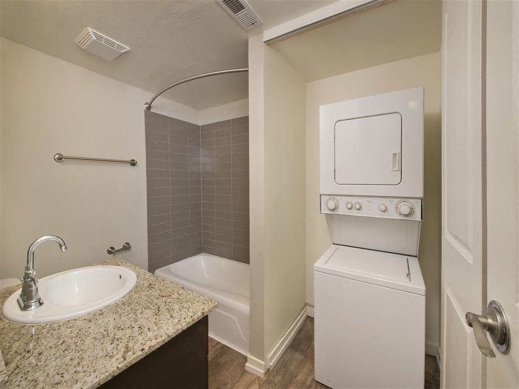In-unit bathroom with a granite vanity, tub/shower, and a stacked washer and dryer.
