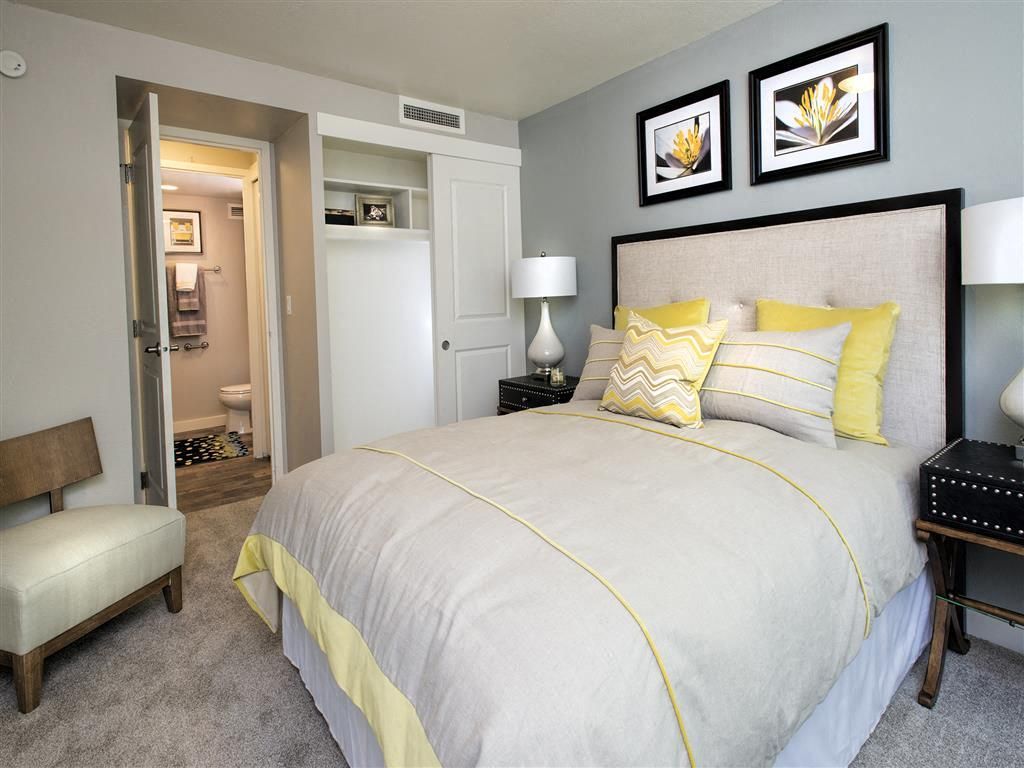 Bedroom in an apartment with a large bed, two lamps, and an open closet; bathroom visible.