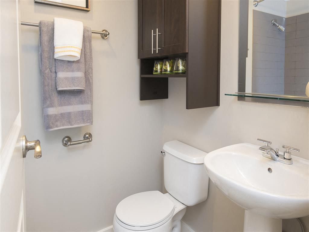 Bathroom with toilet, pedestal sink, mirror, and wall cabinet.