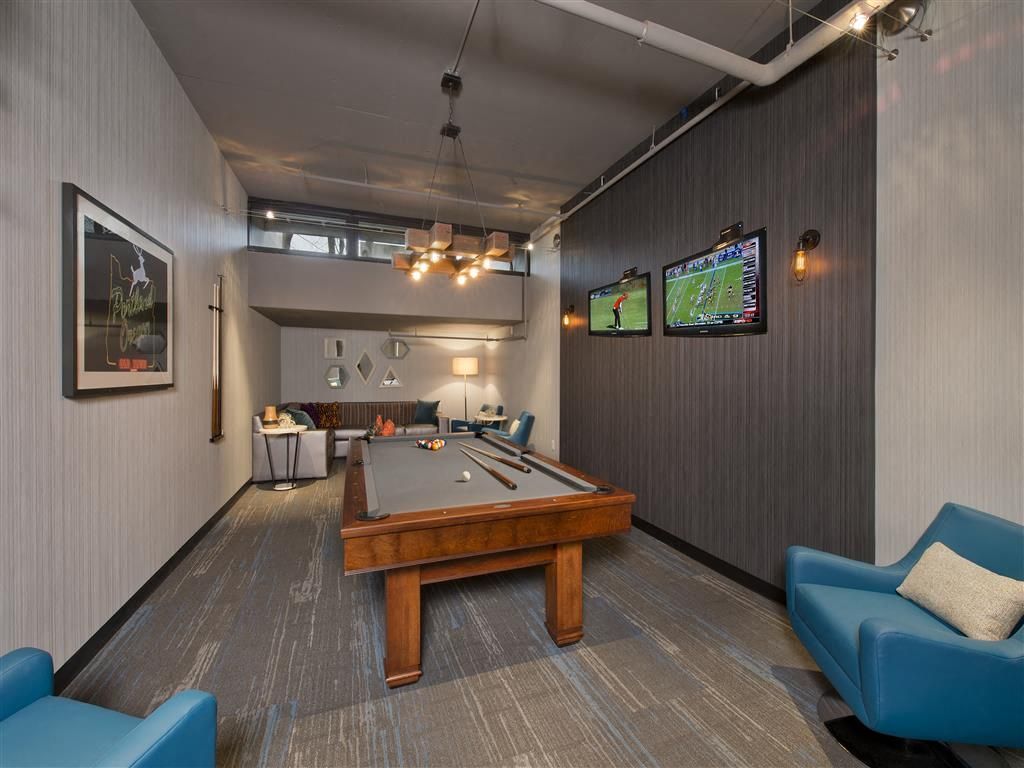 Indoor community game lounge with pool table, seating, and wall-mounted TVs.