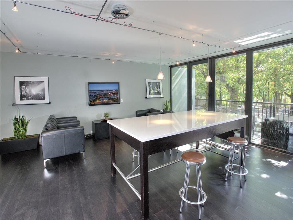 Modern community lounge with a high white table, stools, and large glass doors to a balcony.
