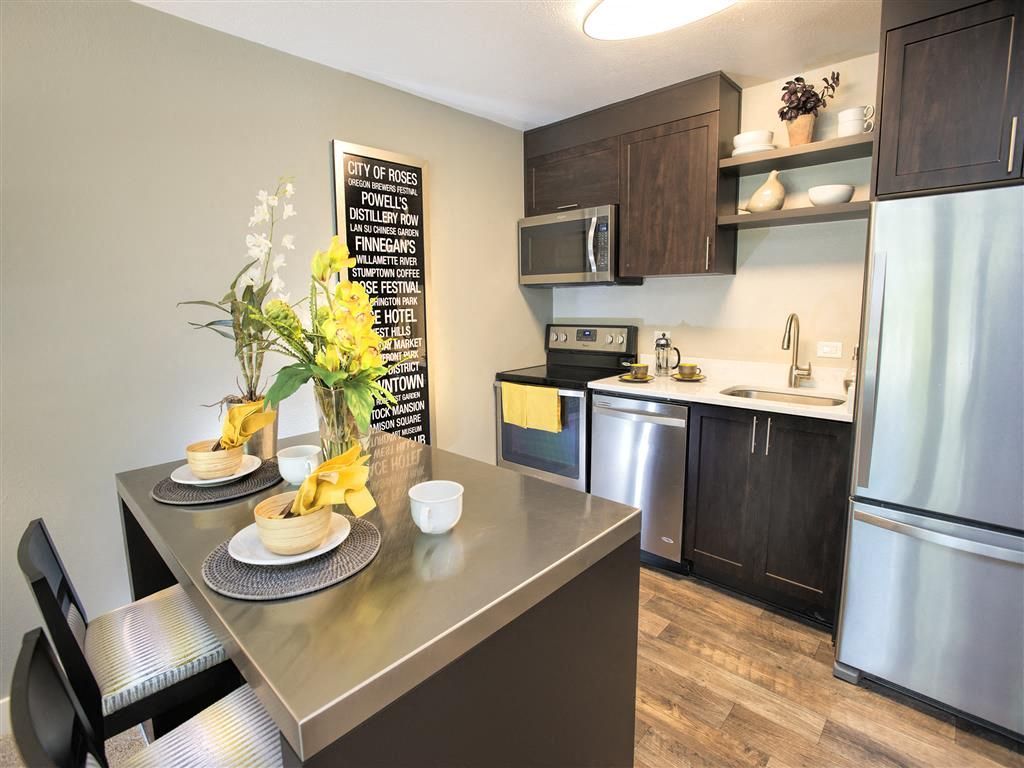 Kitchen in a modern apartment with dark wood cabinets, stainless steel appliances, and a dining island.