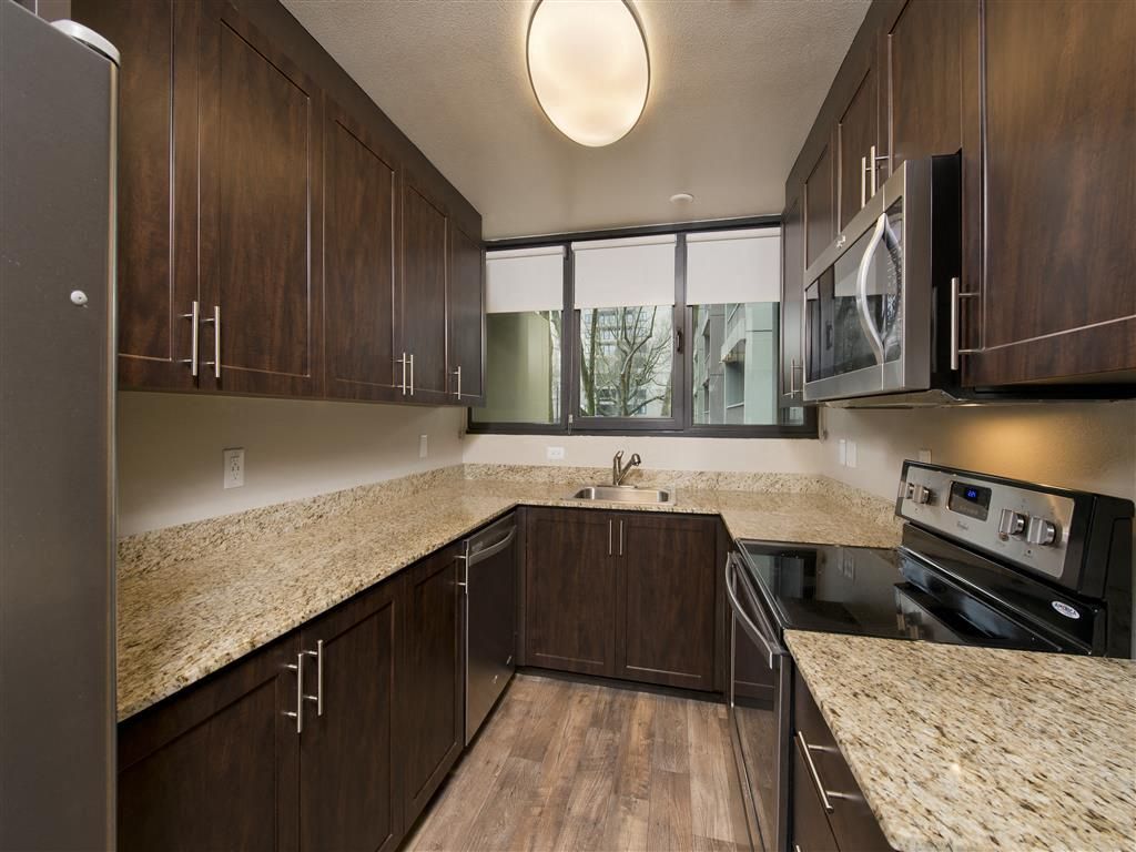 U-shaped kitchen with dark wood cabinets, granite countertops, stainless steel appliances, and a window above the sink.