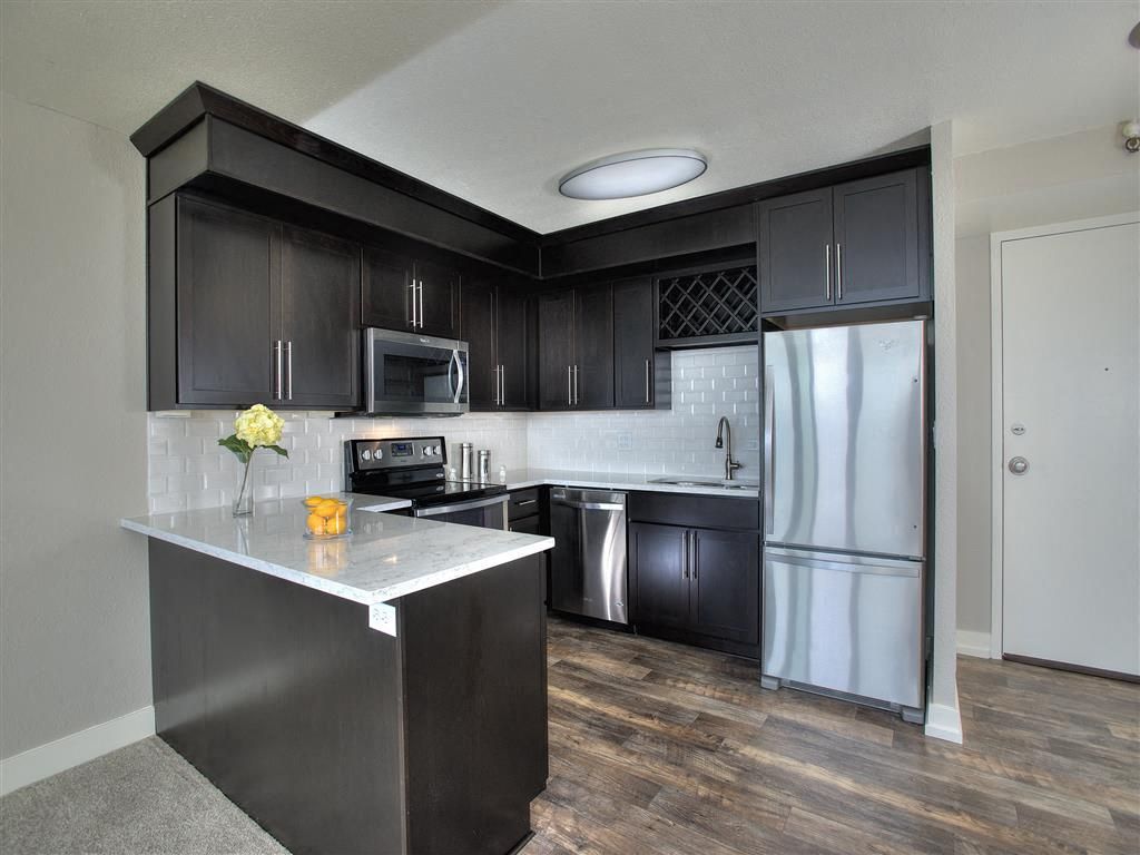 Modern apartment kitchen with dark cabinets, white quartz countertops, and stainless steel appliances.