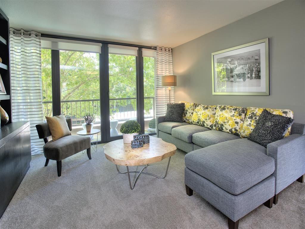 Living room in an apartment with a gray sectional, round wood coffee table, and large windows.