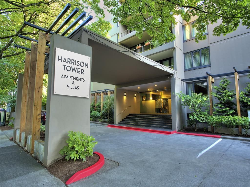 Entrance to Harrison Tower Apartments & Villas with sign and steps, surrounded by trees.