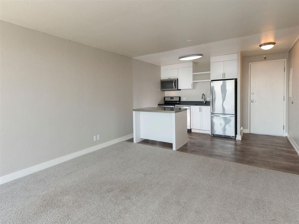Open-plan apartment kitchen with island, white cabinets, and stainless-steel appliances.