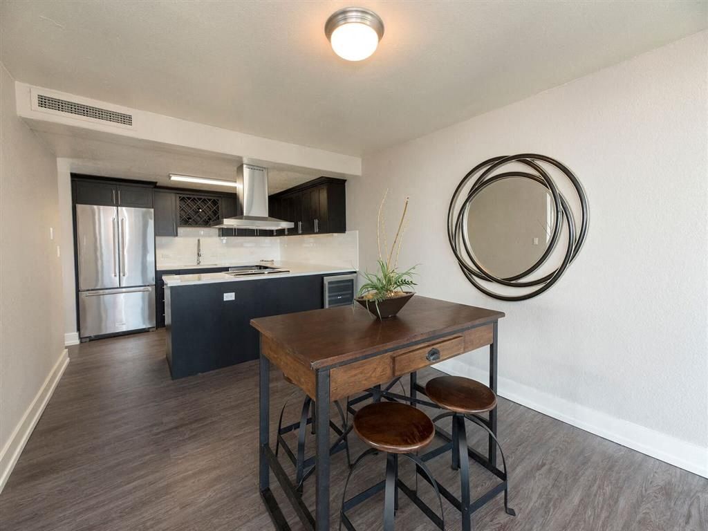 Open-plan kitchen and dining area with stainless fridge, dark cabinets, and a wooden table with stools.