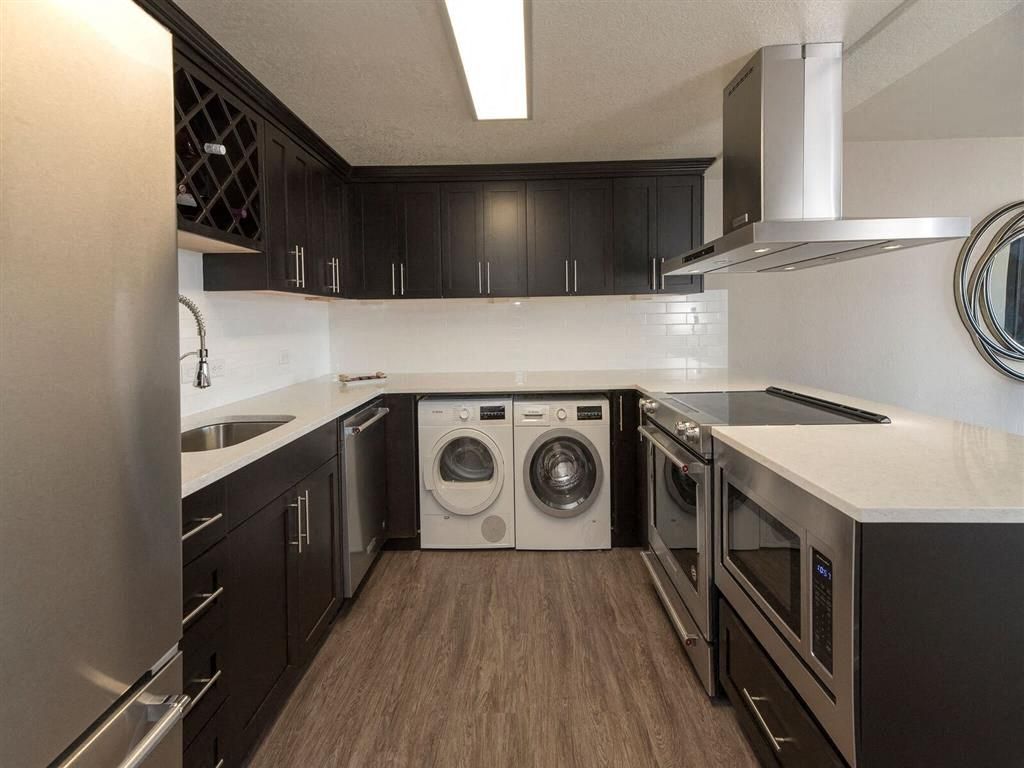 Modern U-shaped kitchen with dark cabinets, white countertops, stainless steel appliances, and a stacked washer/dryer.