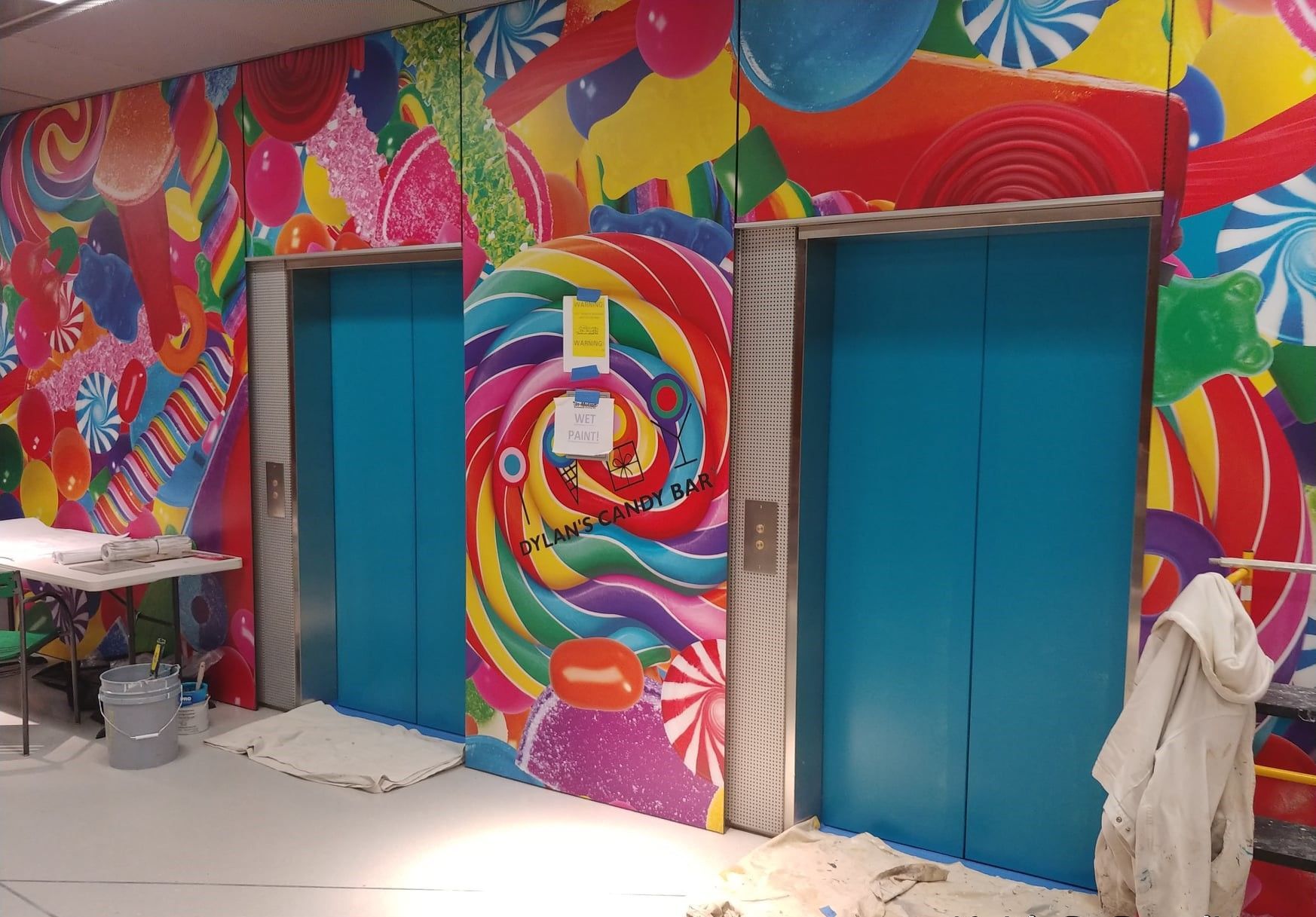 Two blue elevators with a colorful mural on the wall behind them.