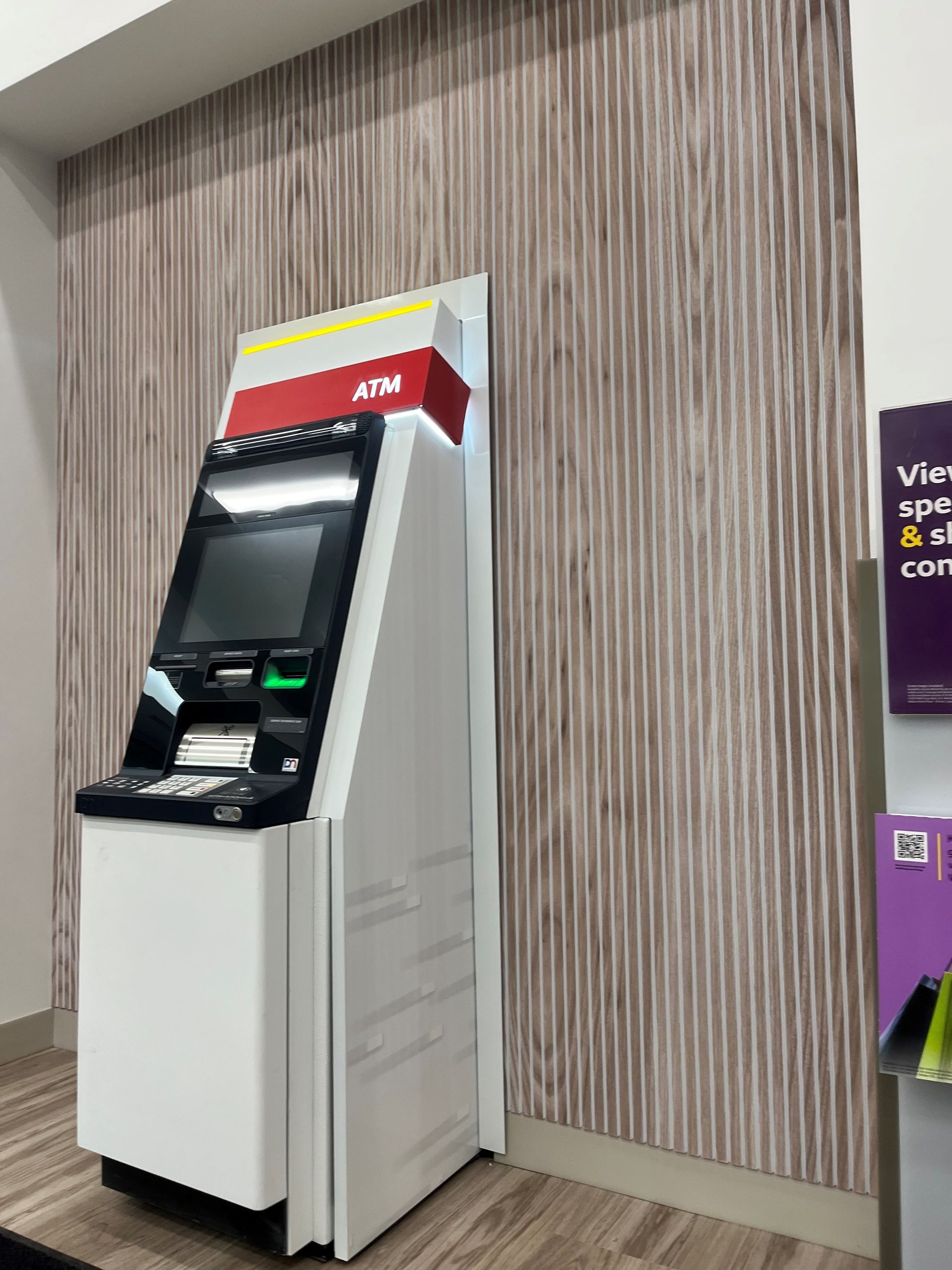 An ATM machine is sitting in a room next to a wall.