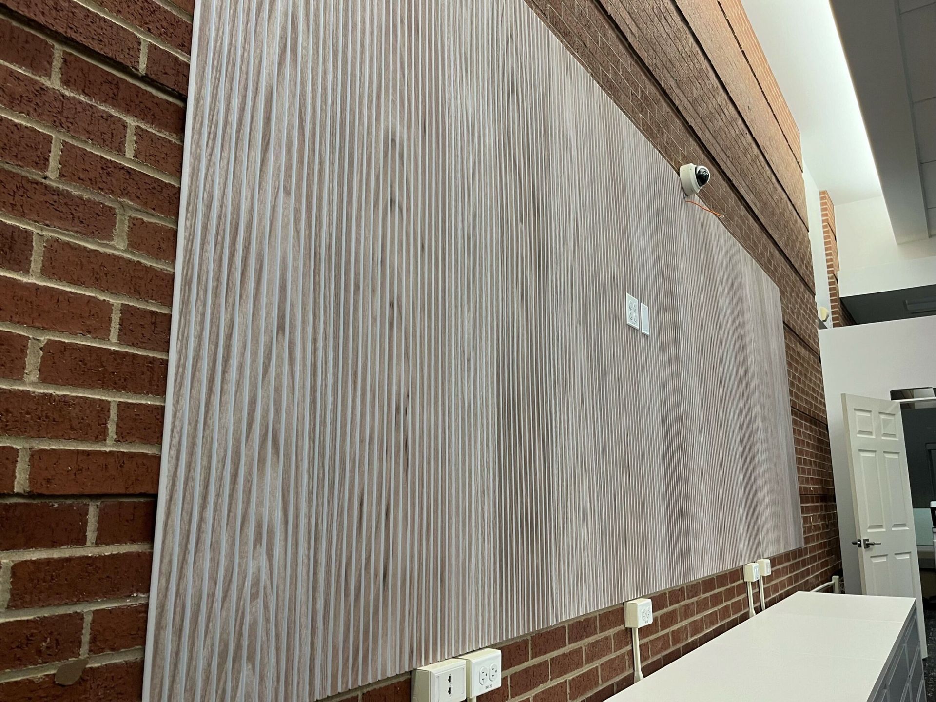 A large piece of wood is hanging on a brick wall.