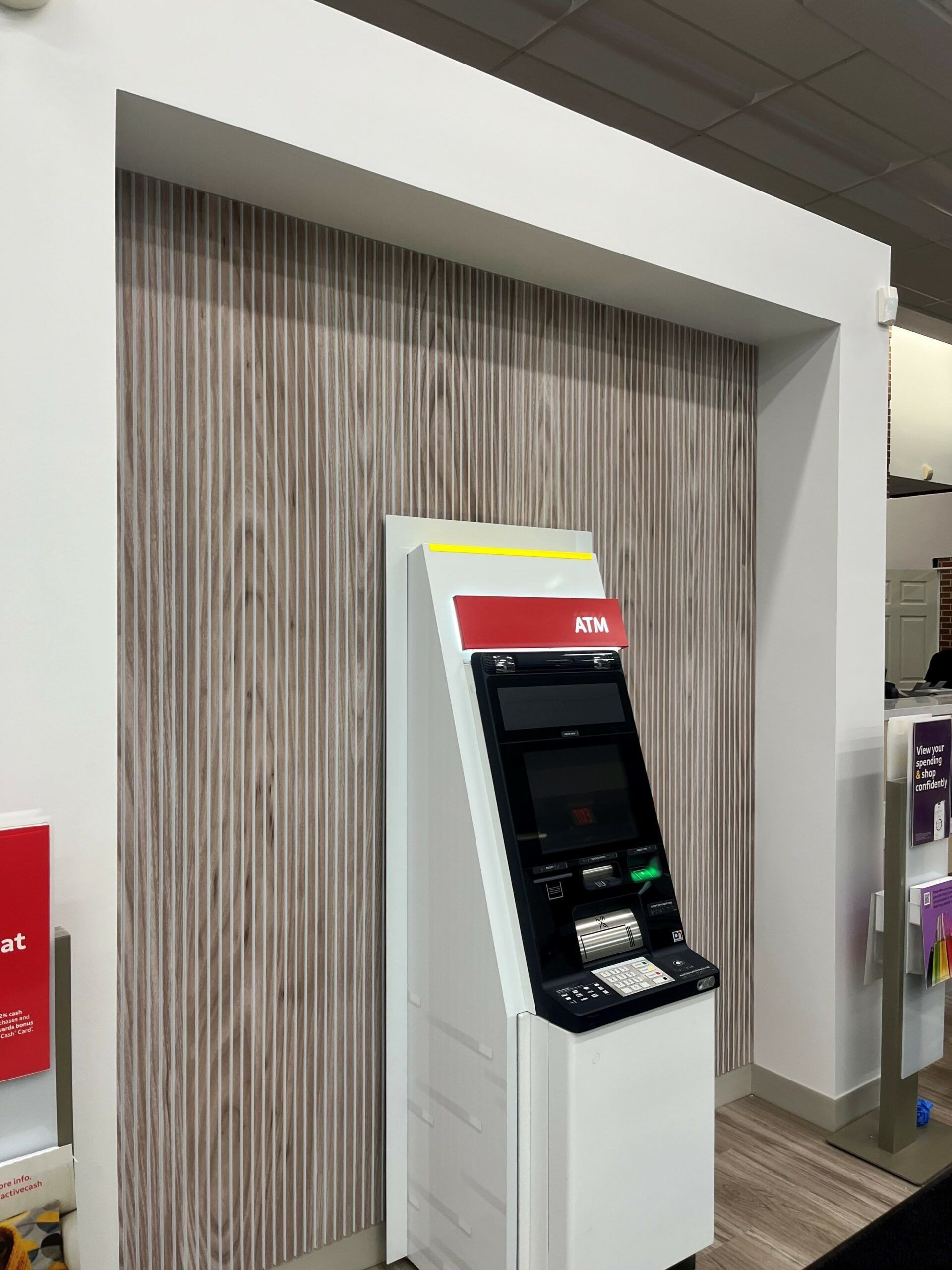 A white ATM machine is sitting in front of a wooden wall.