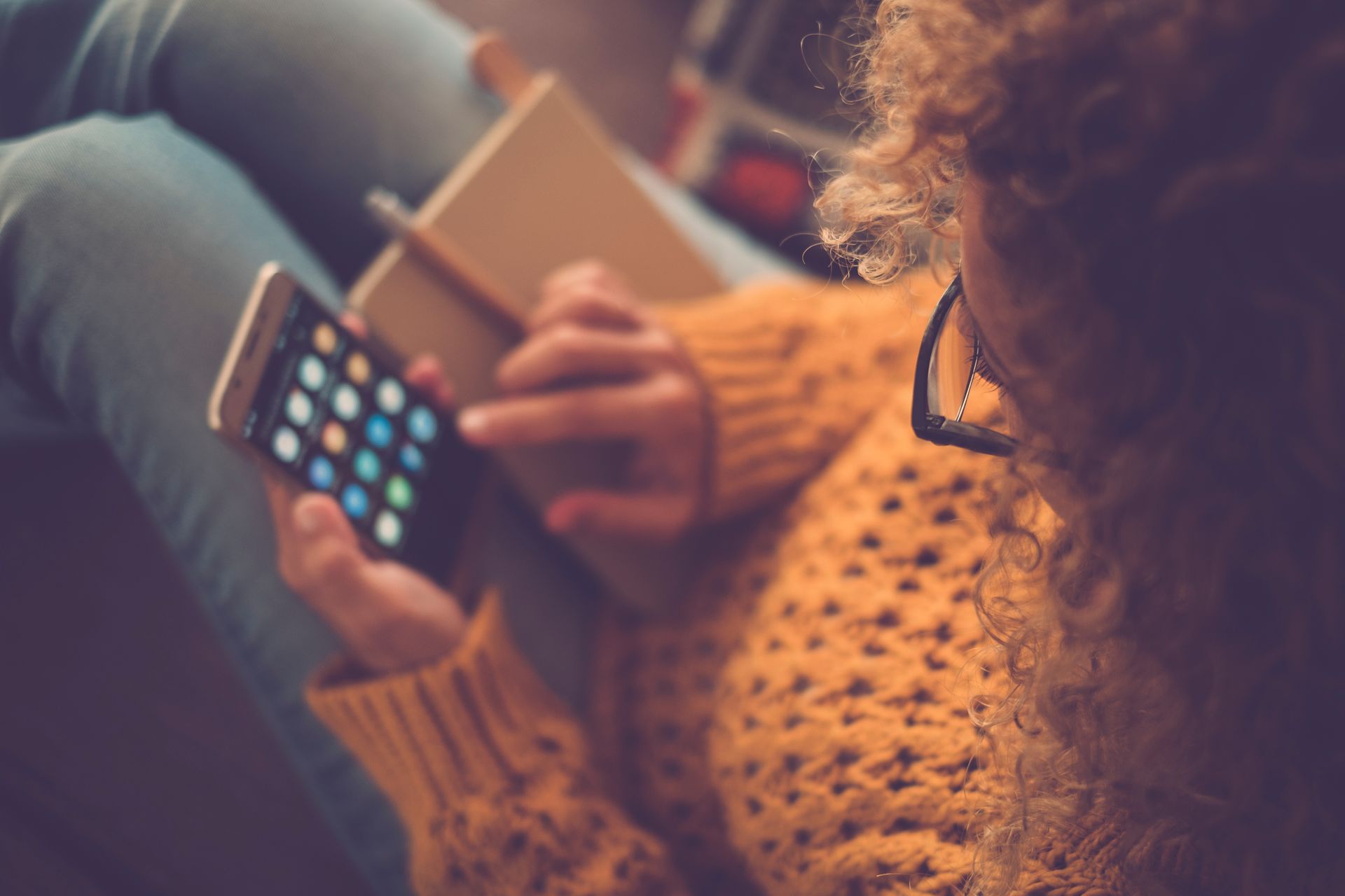 Person in a mustard sweater using a smartphone while sitting on a couch