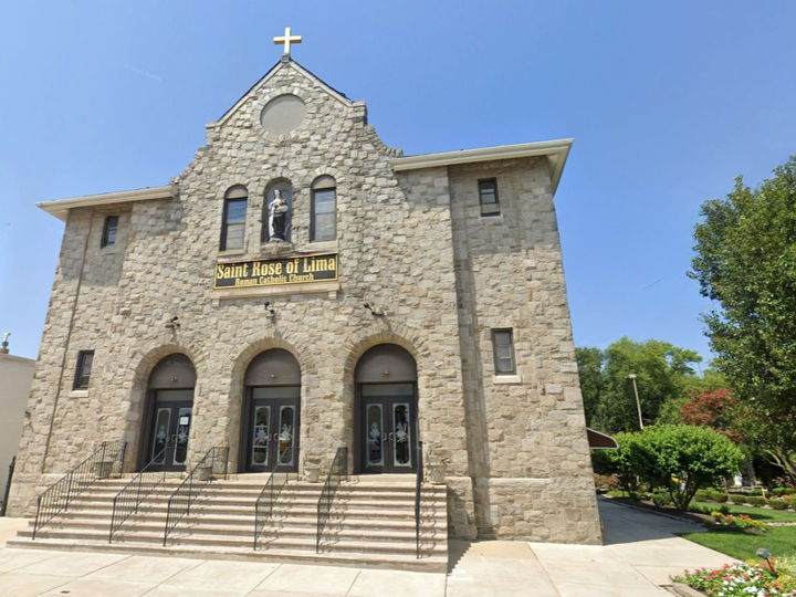 Stone church facade with cross, arched windows, and steps under a clear blue sky