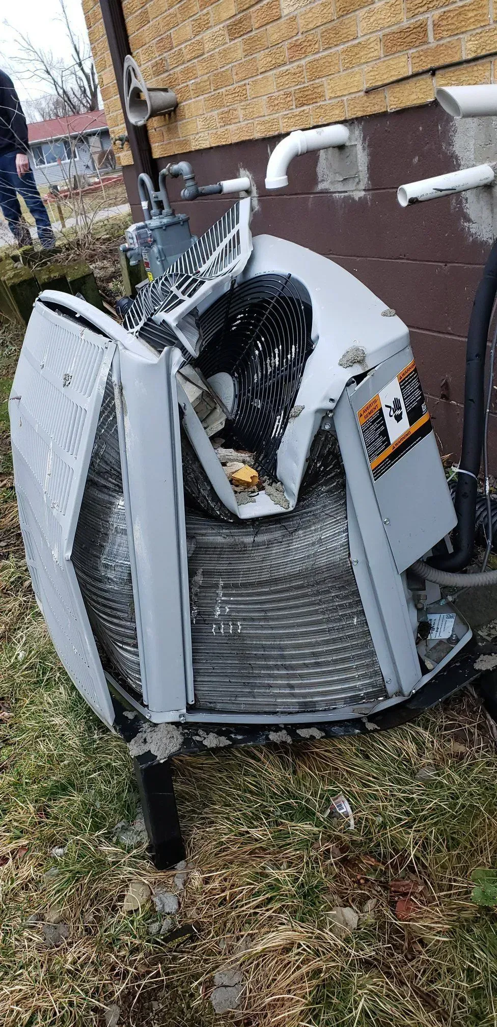 Damaged outdoor air conditioning unit next to a brick building.