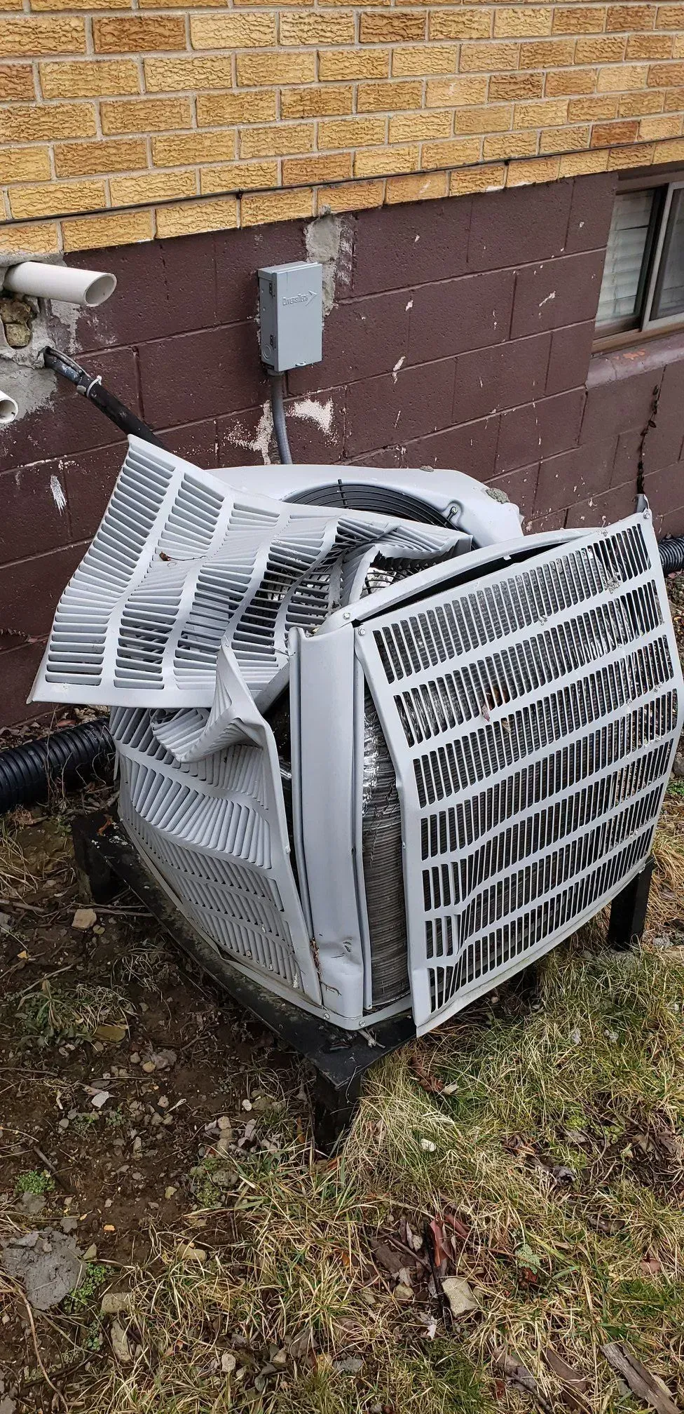 Damaged air conditioning unit outside a brown building. Metal panels are bent and open.