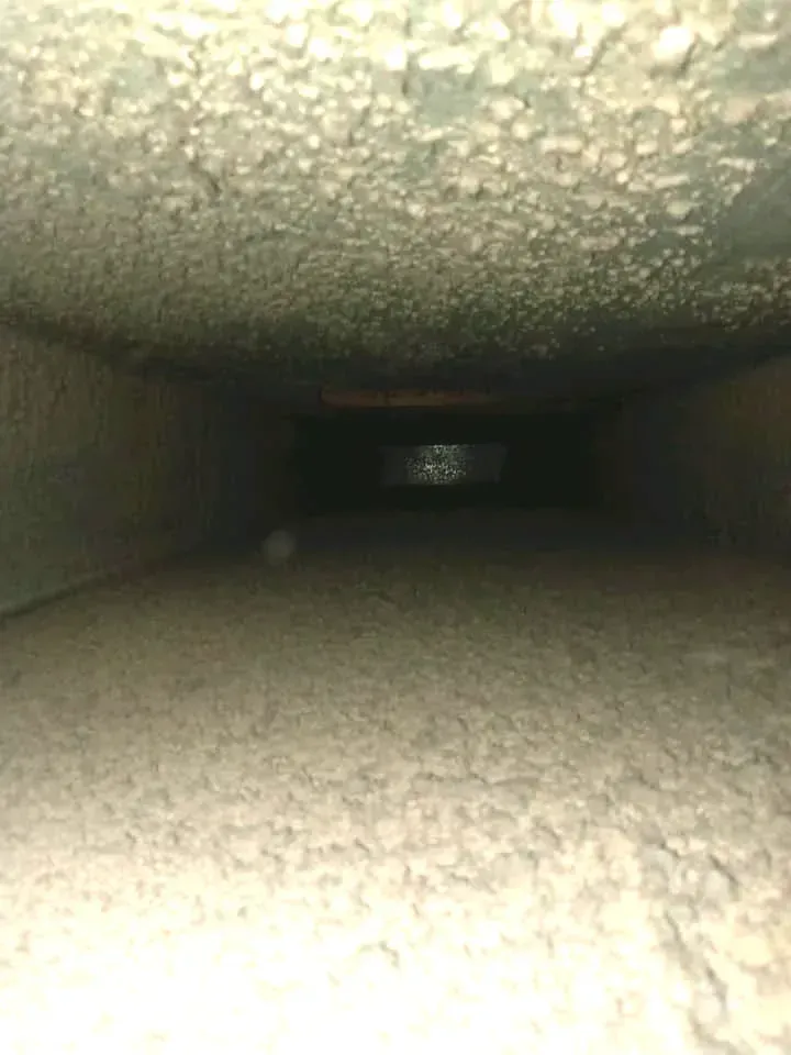 Interior of a rectangular air duct coated with a thick layer of dust. The duct interior is dark and the end is out of view.