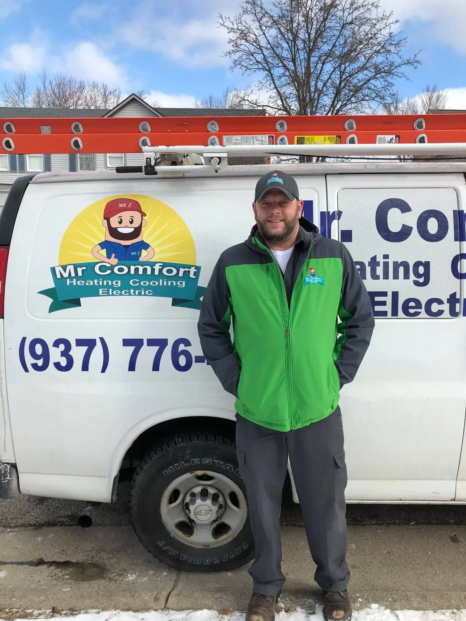 Man standing in front of a white Mr. Comfort van with ladder. He wears a green jacket, gray pants.