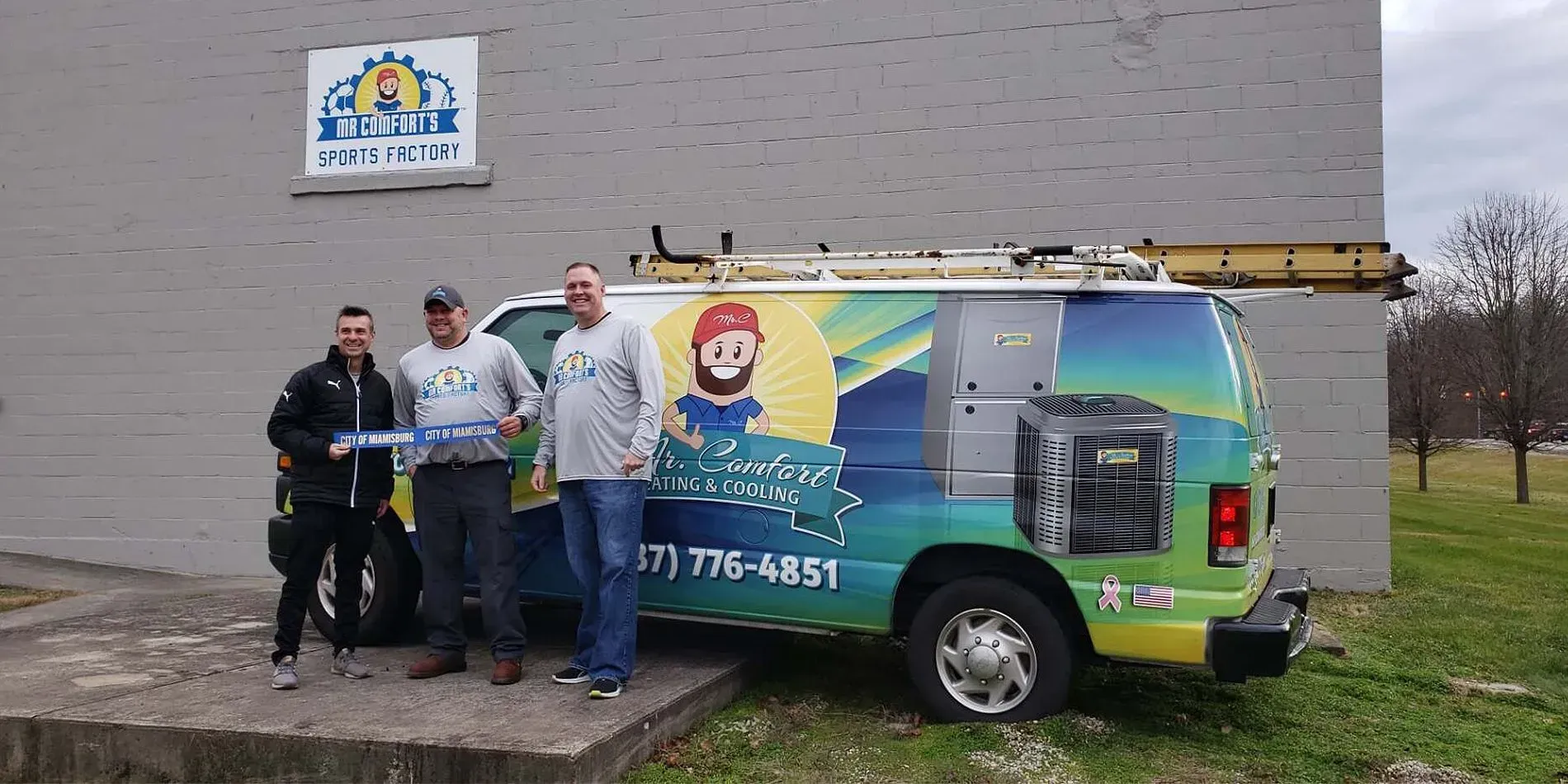 Three men stand with a company van in front of a building. The van is brightly colored.