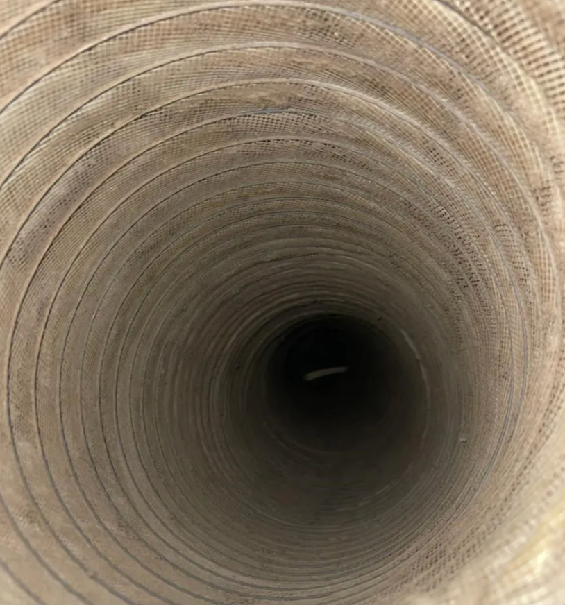 Inside view of a dusty, cylindrical air duct, fading into darkness.