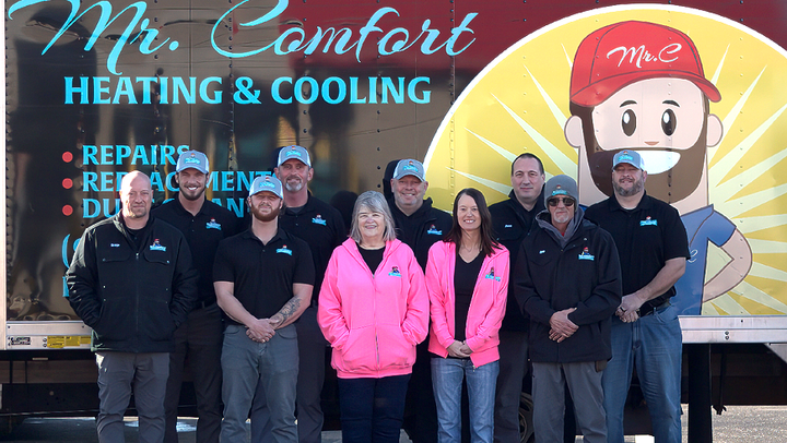 Mr. Comfort Heating & Cooling team standing in front of their truck. Logo: cartoon man. People wear branded shirts and hats.