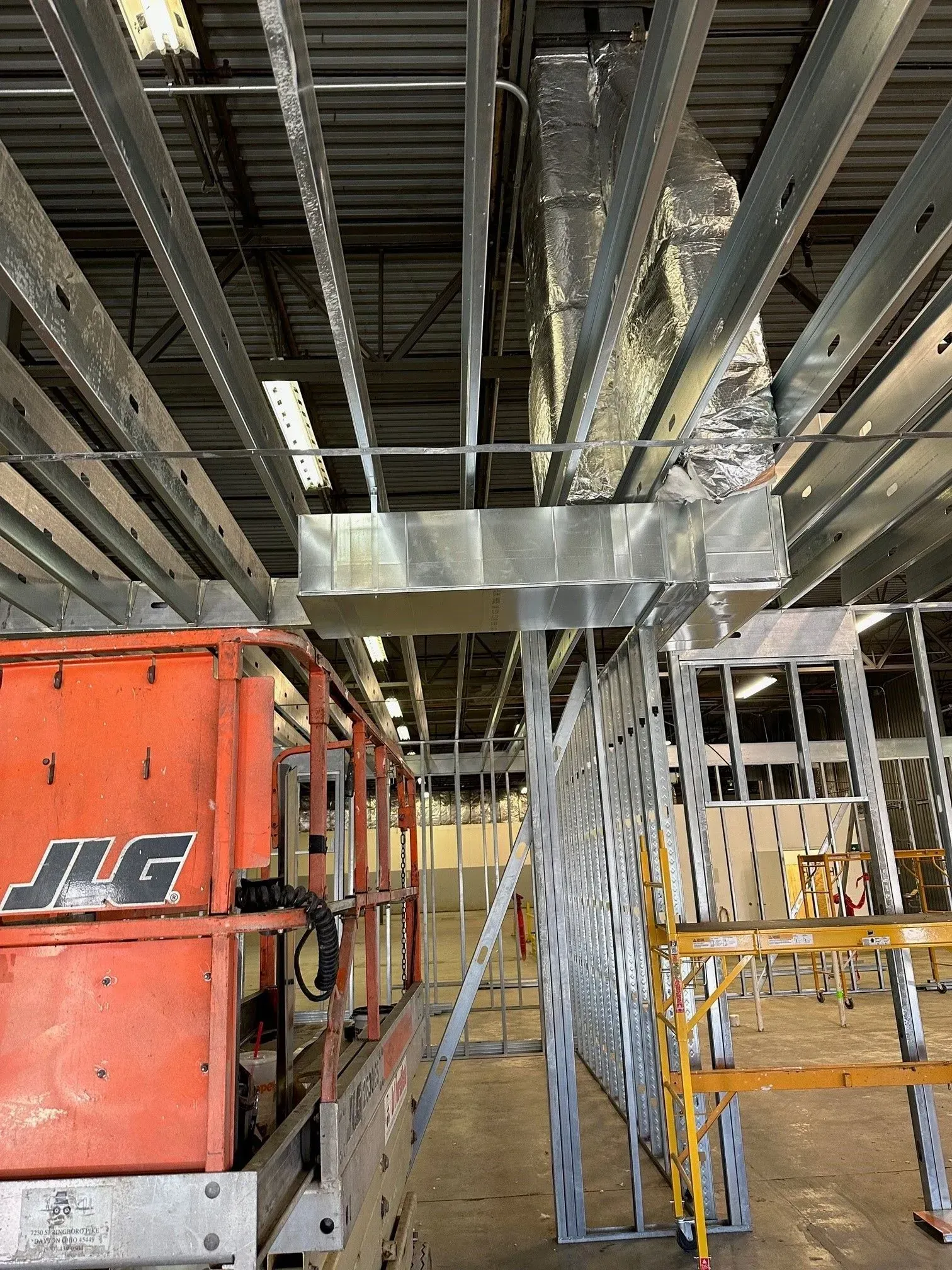 Orange lift next to a partially constructed building interior with exposed metal framing and HVAC ductwork.