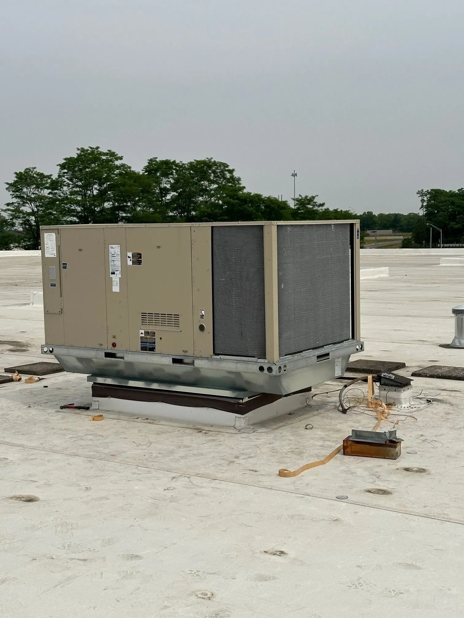 Large HVAC unit on a flat, white roof with visible vents and electrical components, against a cloudy sky.