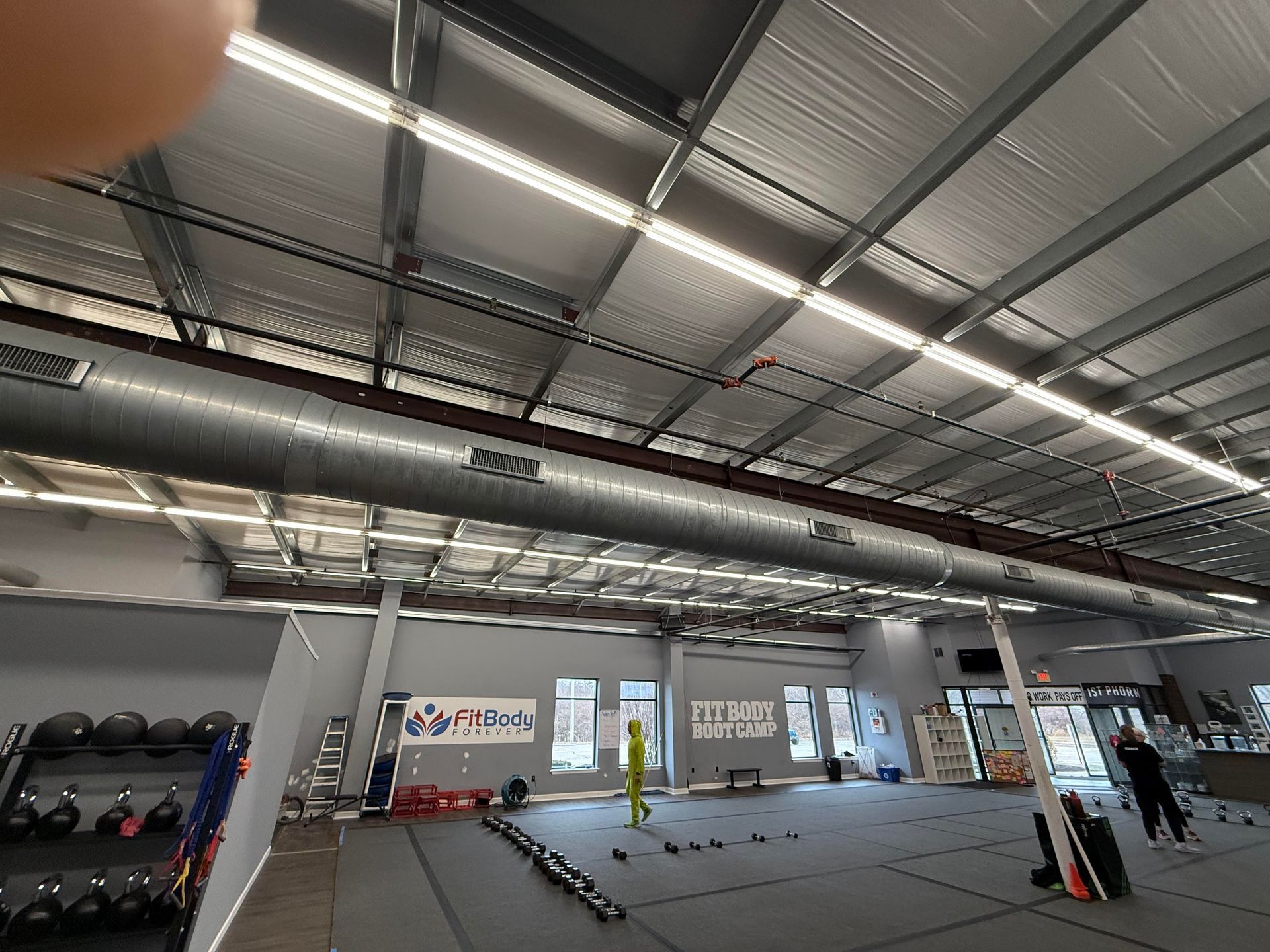 Gym interior with metal roof, lights, exercise equipment, and people.