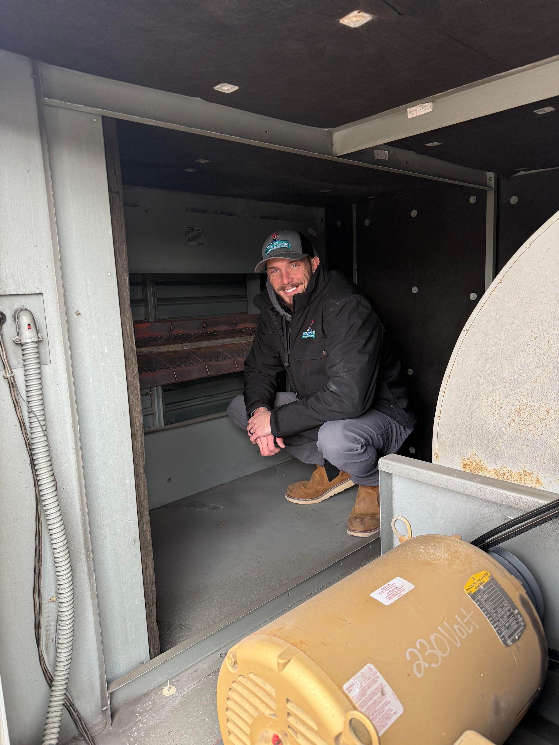 Man squats in a dark compartment, smiling. A large motor sits in the foreground.