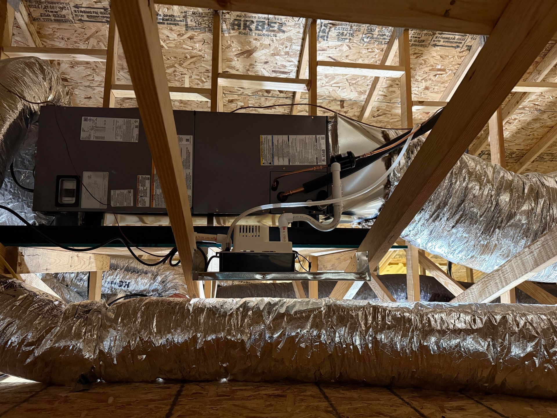 HVAC system in attic: ductwork, unit on wooden beams, insulated silver ducting, exposed framing.