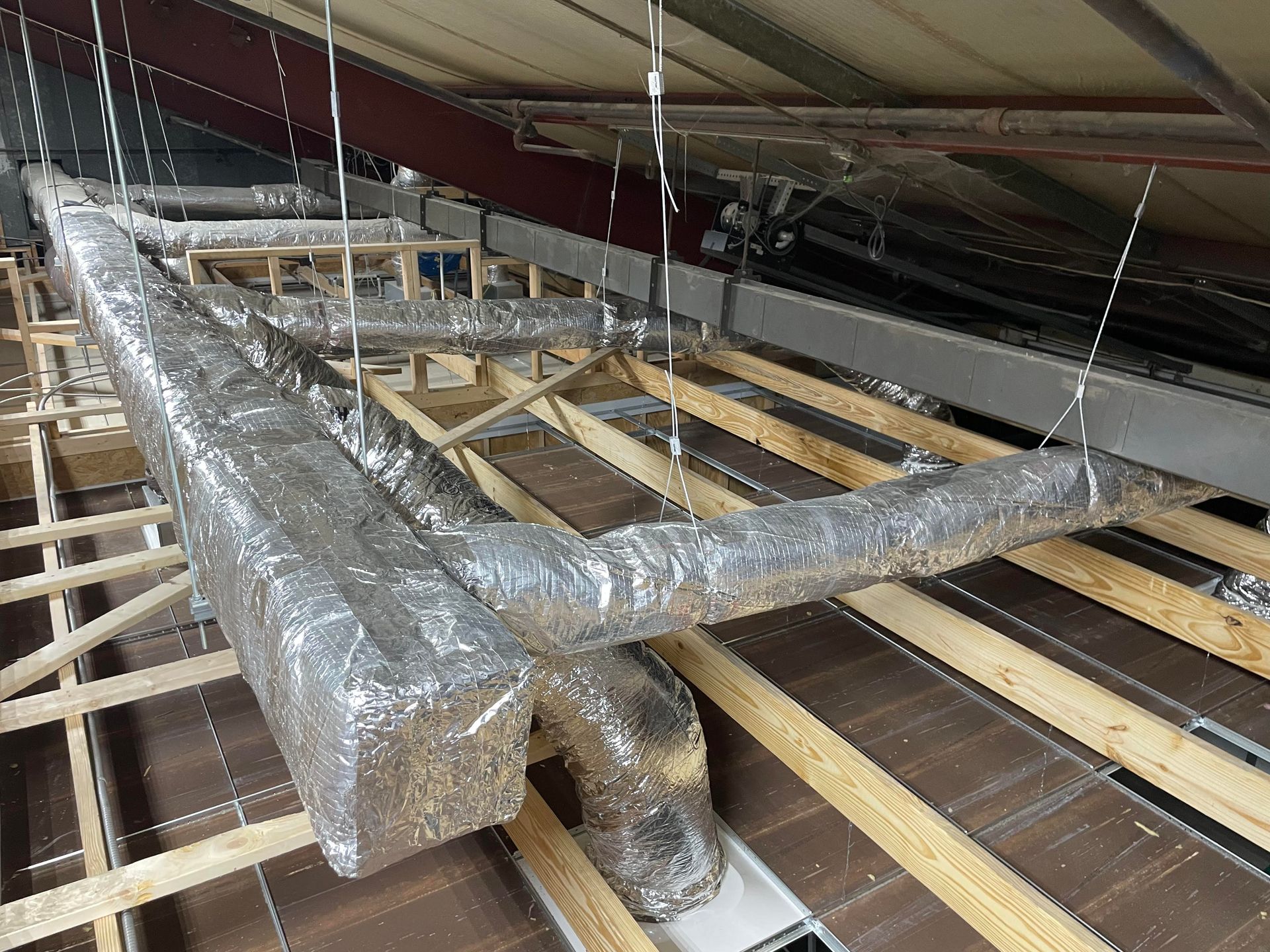HVAC ductwork, wrapped in reflective insulation, suspended from a wooden ceiling structure.