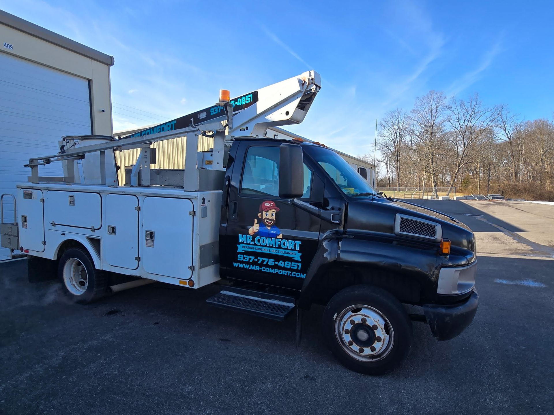 Black and white utility truck with an aerial lift parked outdoors; sunny day.