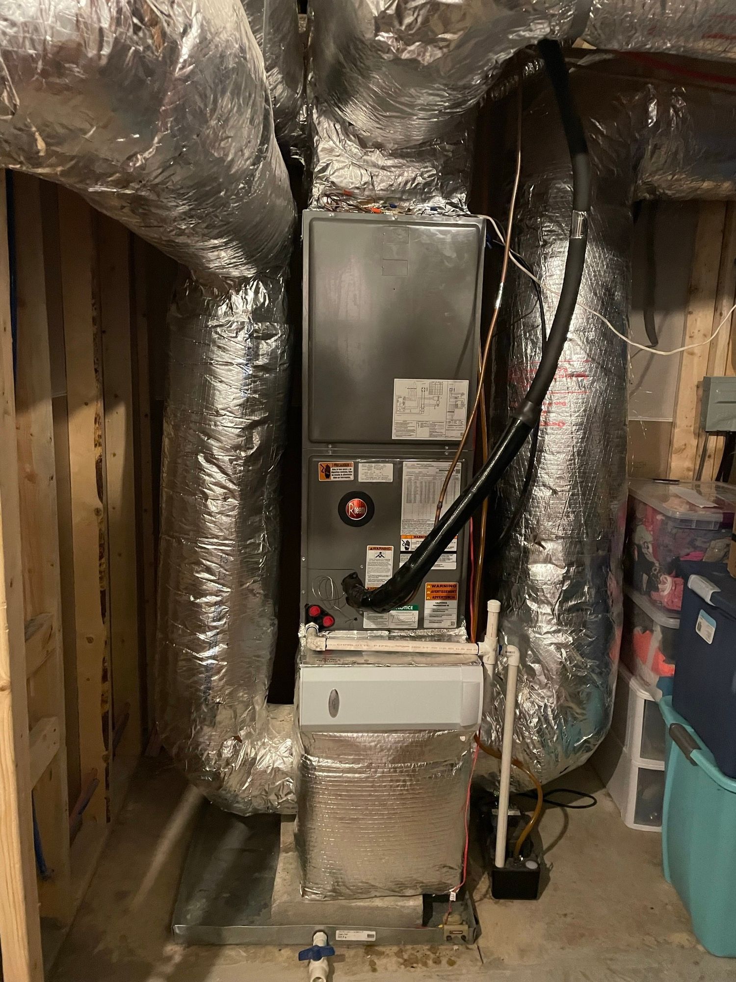 An air conditioner is sitting in a basement surrounded by ducts.