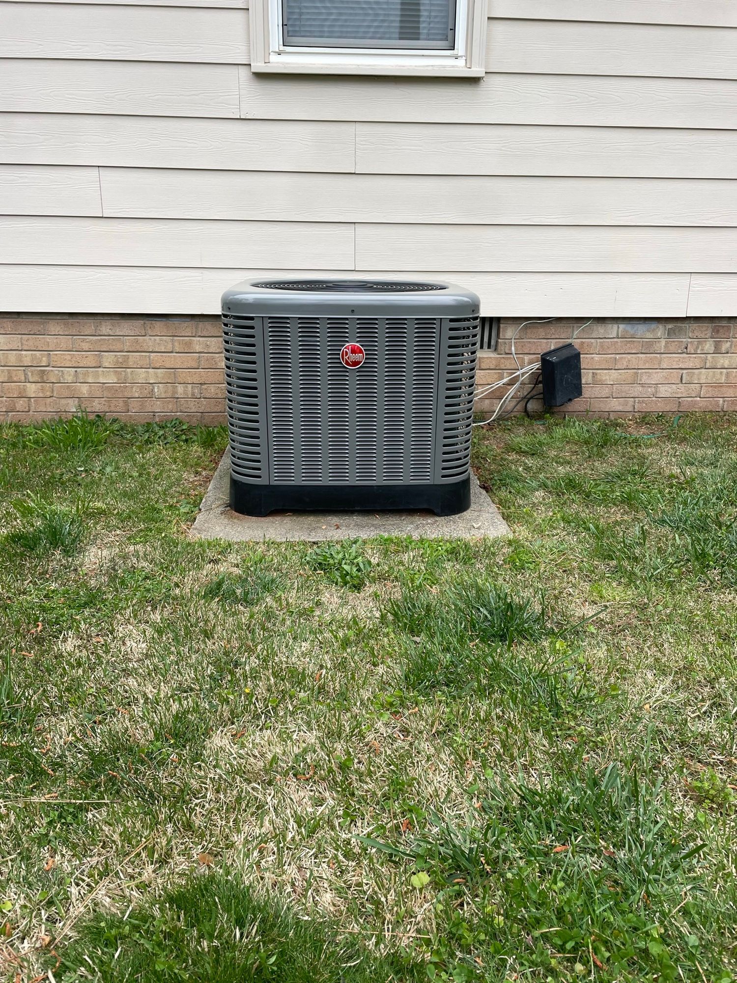 An air conditioner is sitting in the grass in front of a house.