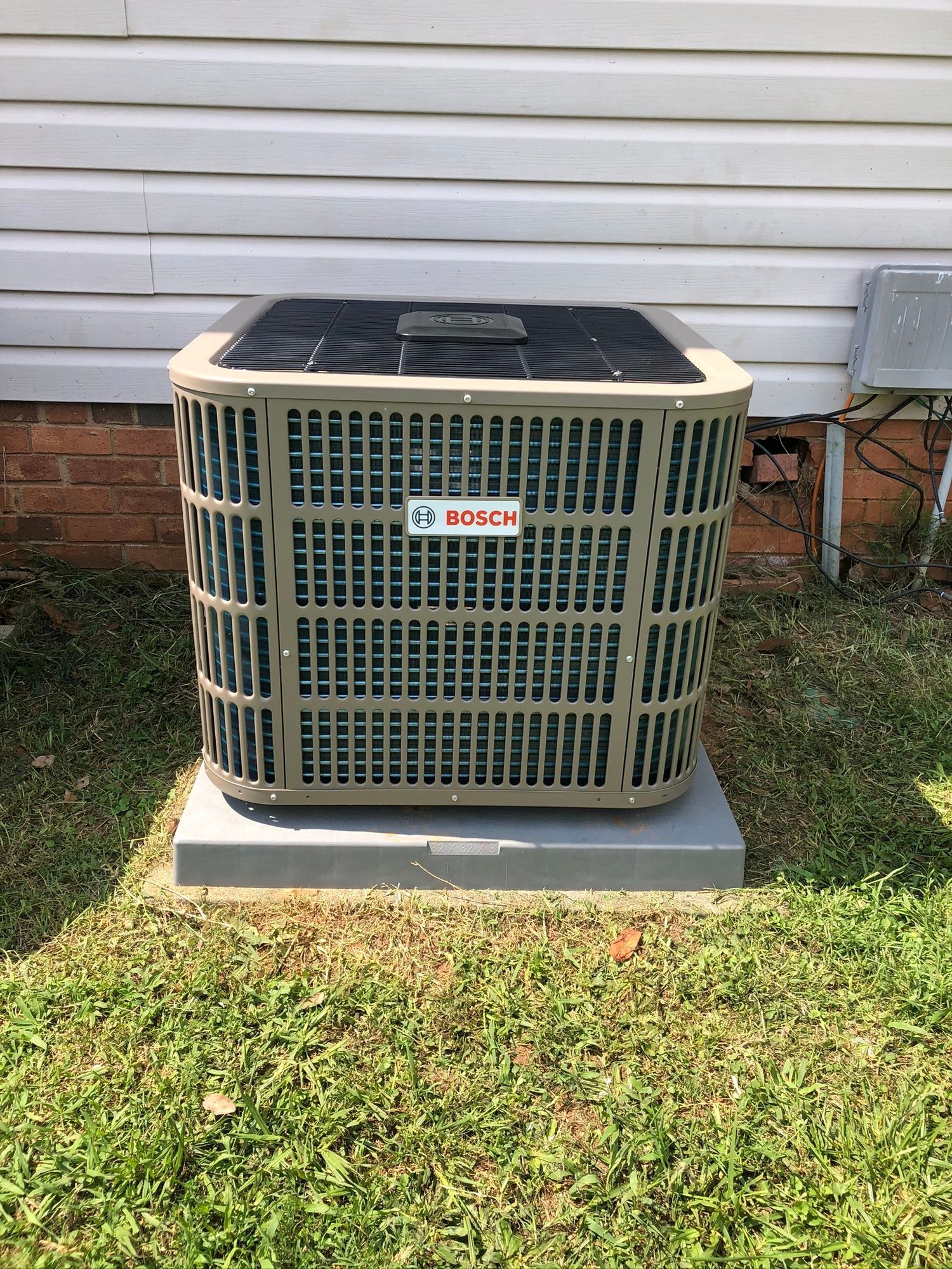 A large air conditioner is sitting in the grass in front of a house.