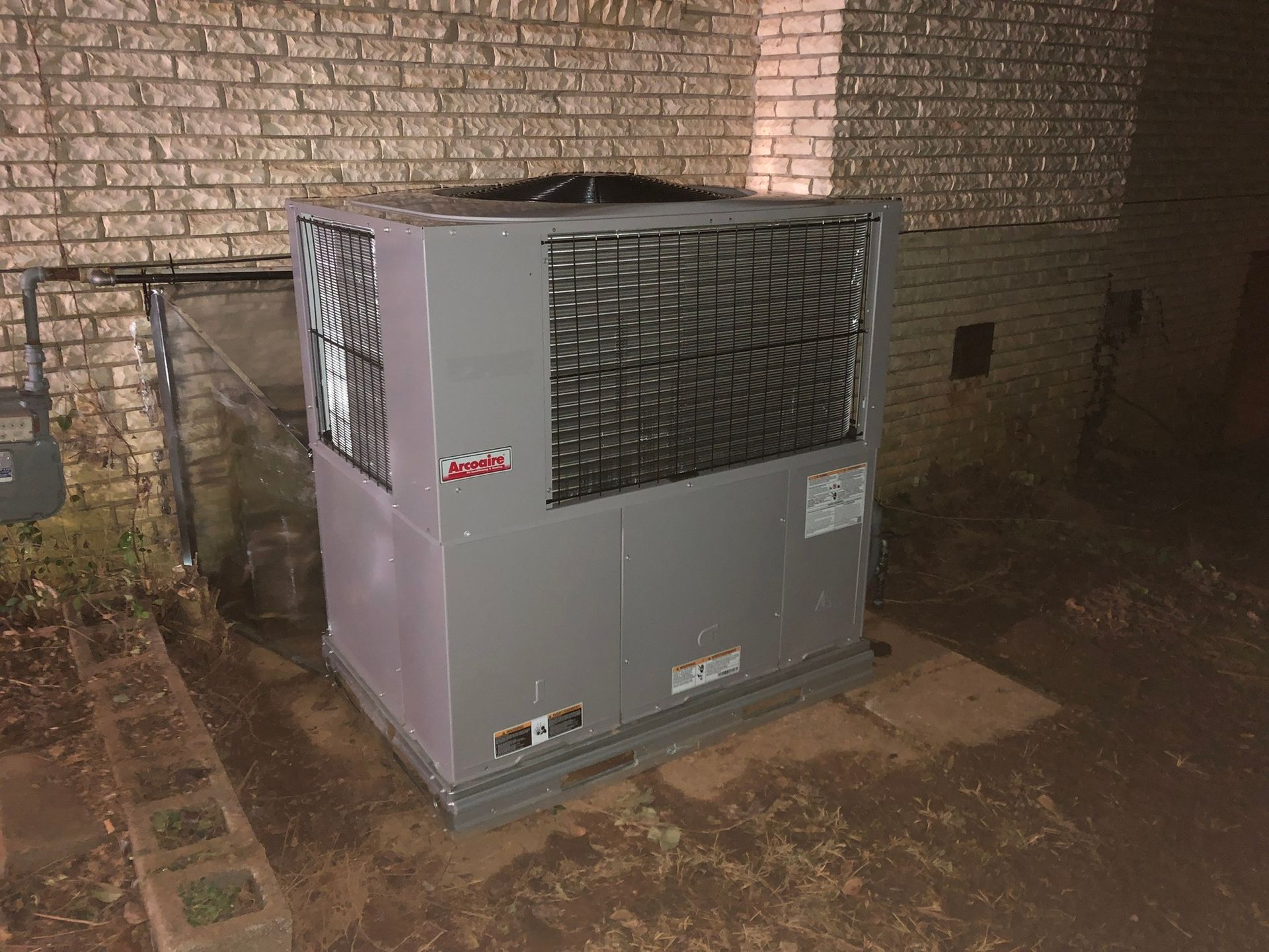 A large air conditioner is sitting outside of a brick building.
