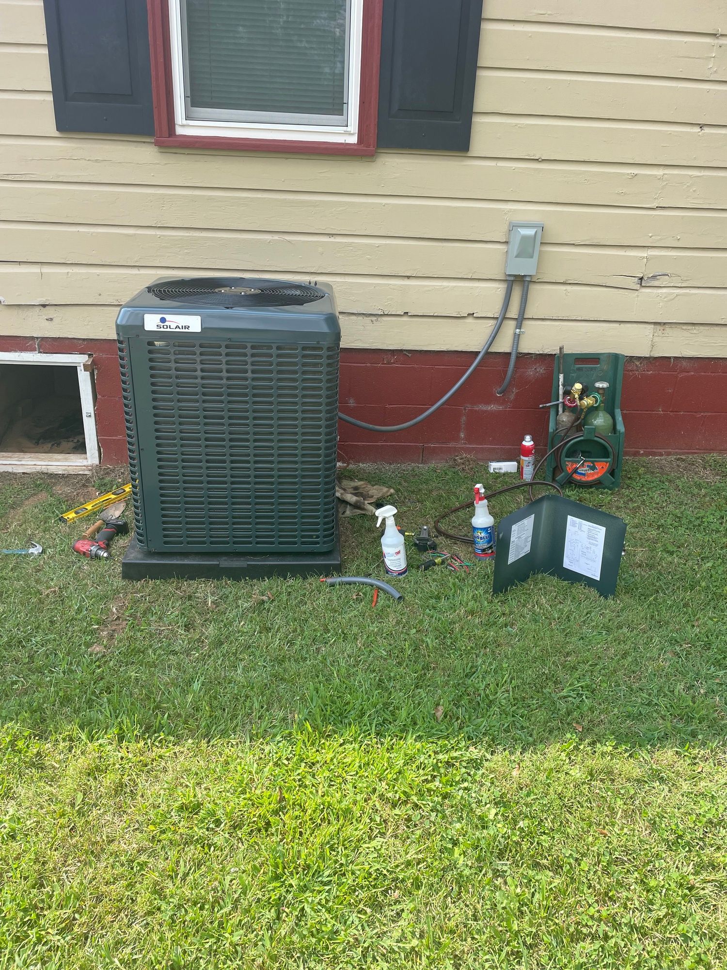 An air conditioner is sitting on the grass in front of a house.