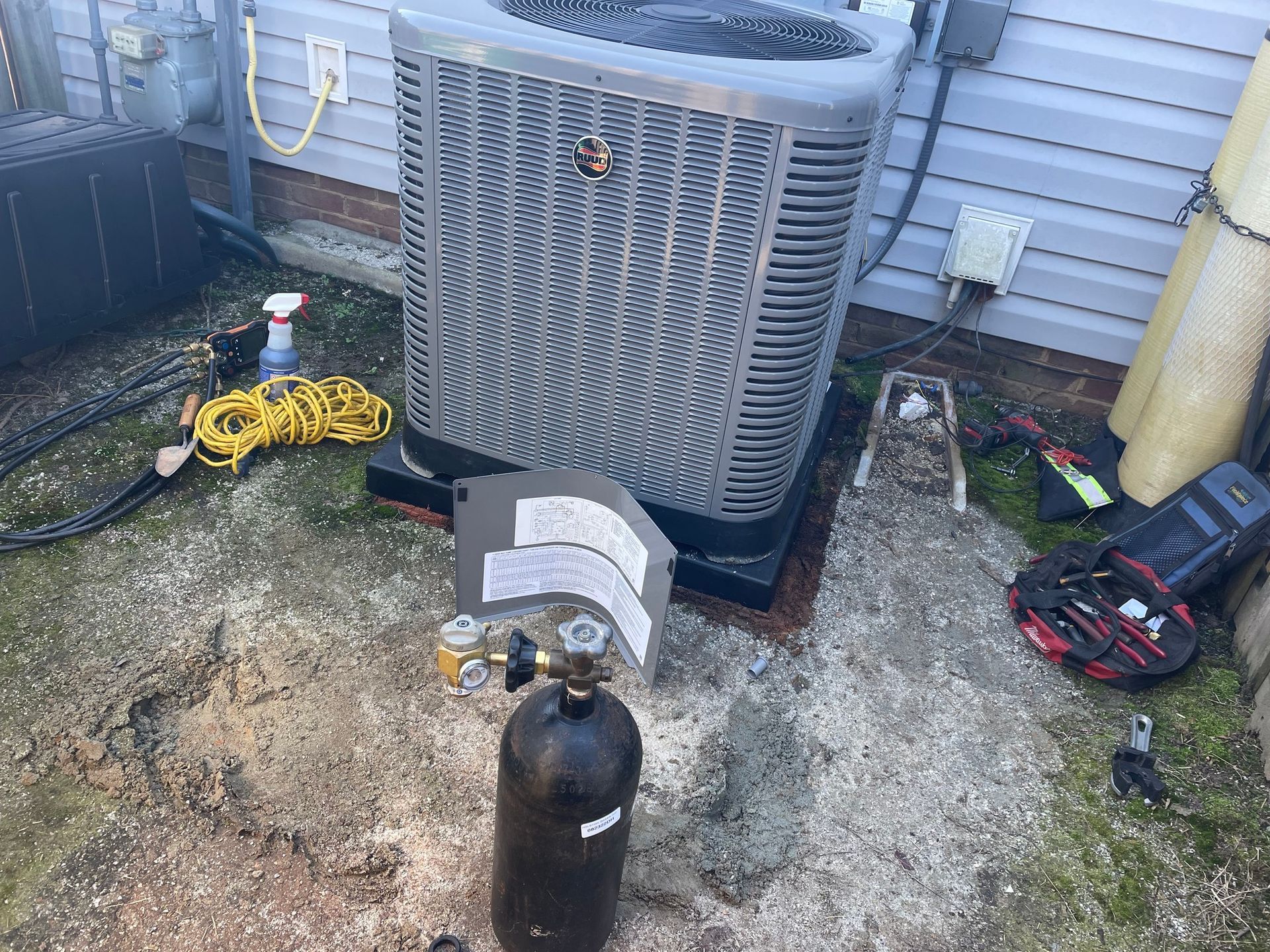 An air conditioner is sitting on the ground next to a bottle of gas.