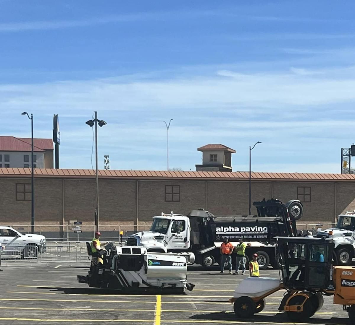 Construction vehicles and workers paving a parking lot on a sunny day.