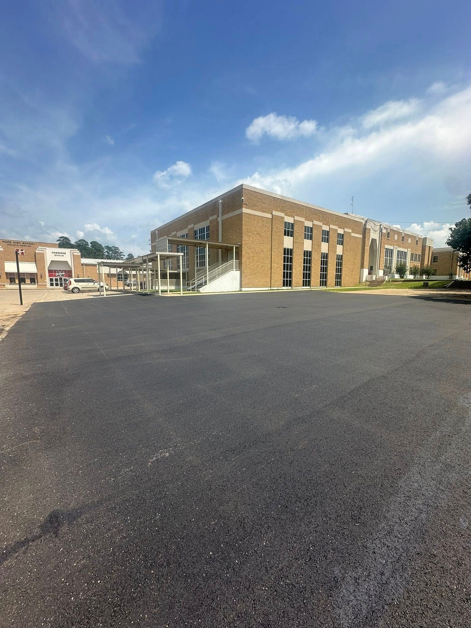 Large building with brick and glass facade, set against a blue sky, asphalt parking lot.