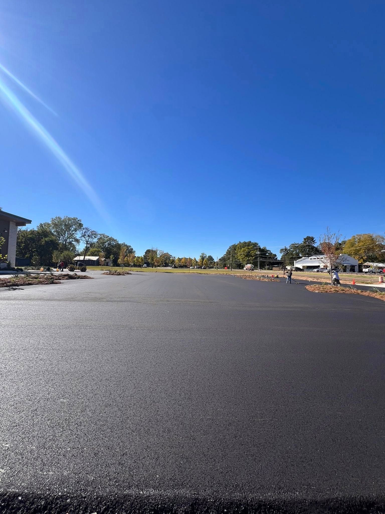Newly paved asphalt parking lot under a bright blue sky.
