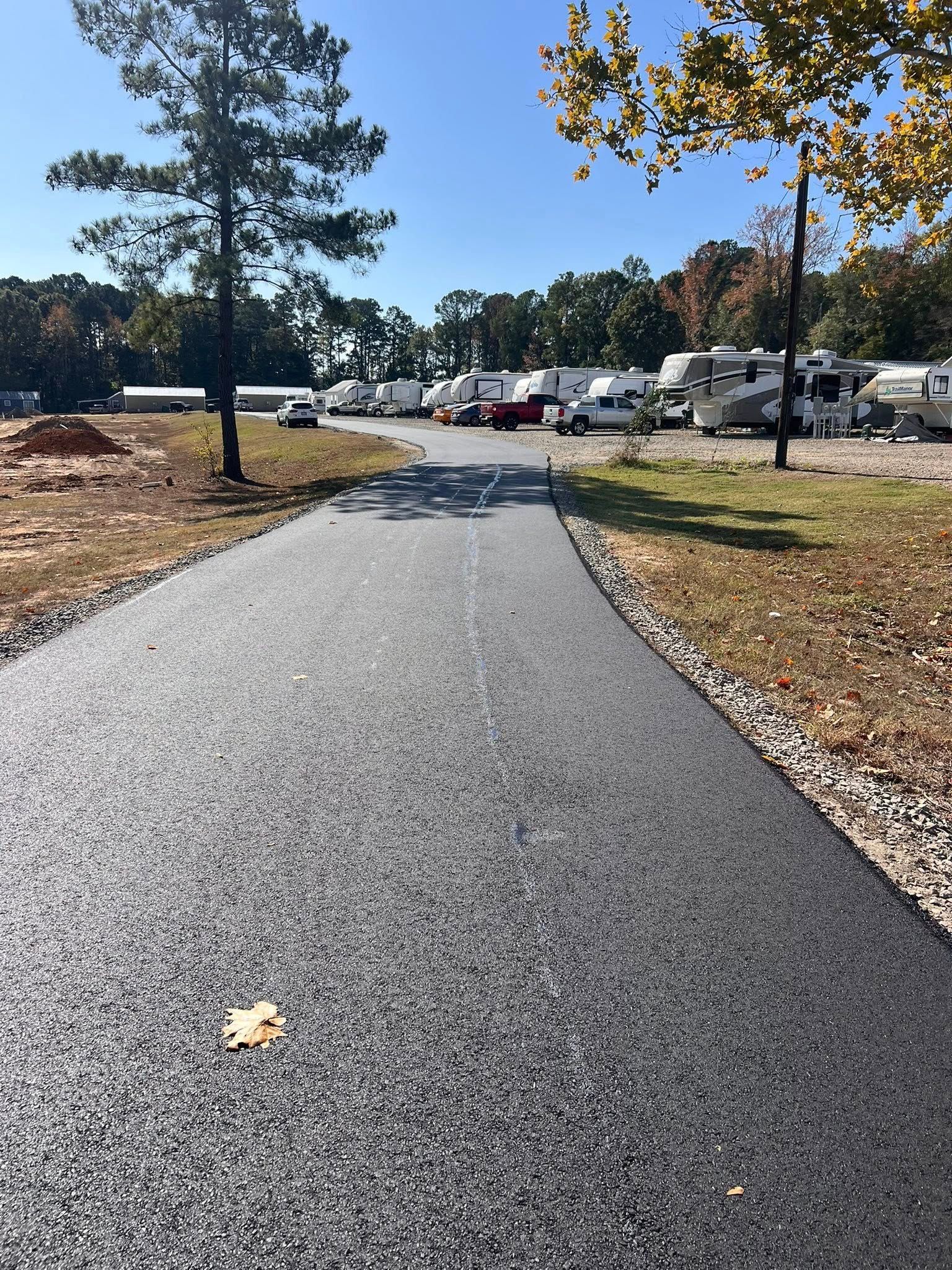 Asphalt path through RV park on a sunny day. Trees and vehicles visible.