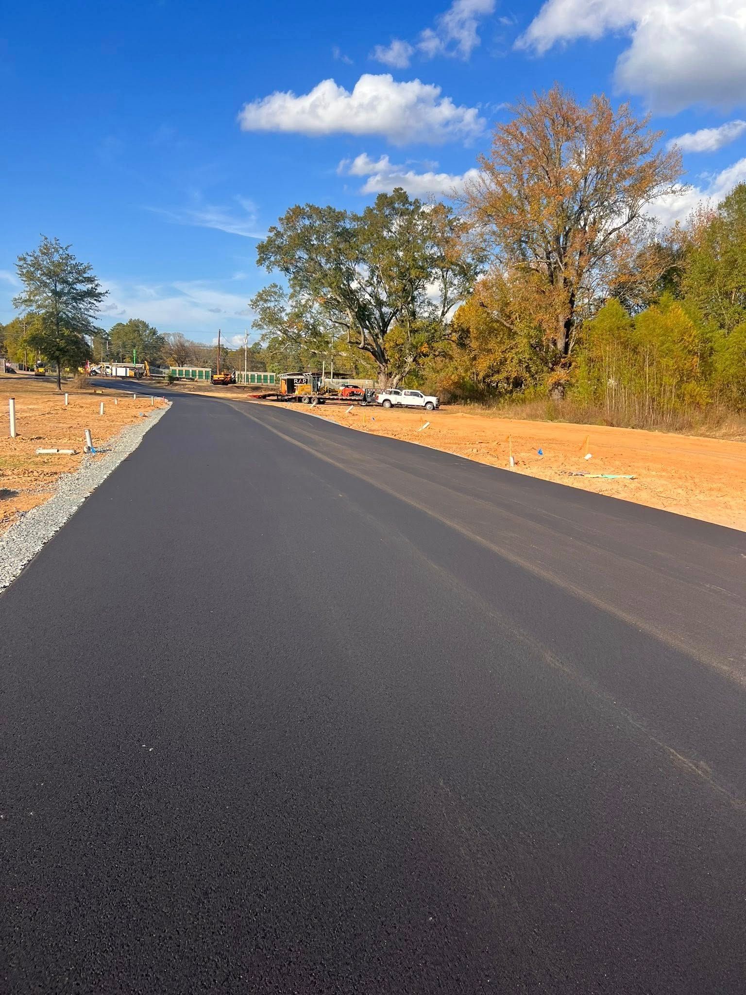 New paved road with construction site on the right and blue sky.