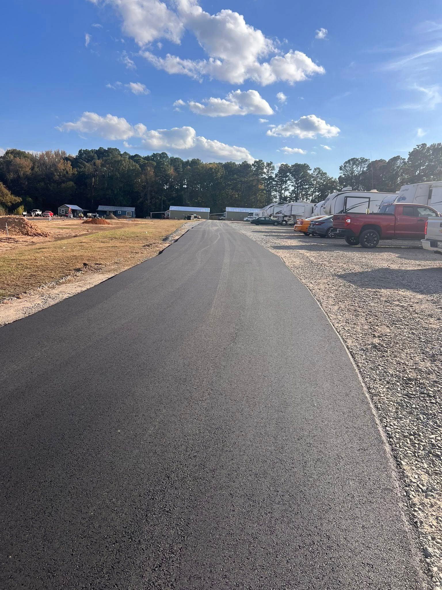 Paved road leads towards a row of RVs on a sunny day.