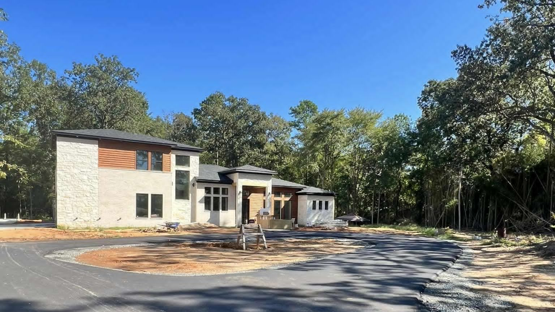 Modern house under construction on a wooded lot, light stone exterior, blue sky.